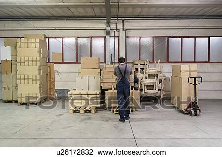Stock Image - Worker lifting boxes onto pallet with pallet jack in factory. Fotosearch