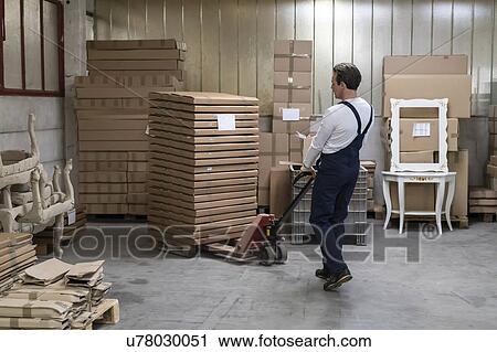 Stock Image - Worker moving pallet of cardboard boxes with pallet jack in factory. Fotosearch