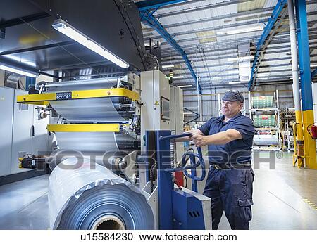Stock Image - Worker moving rolls of food packaging material in print factory. Fotosearch