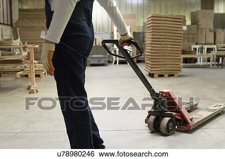 Stock Photograph - Worker pulling pallet jack in factory. Fotosearch