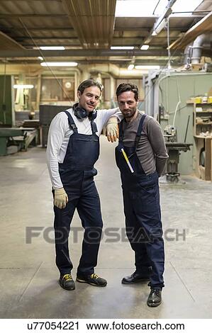 Stock Image - Worker resting arm on colleague's shoulder in factory. Fotosearch