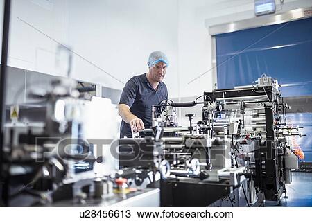 Stock Image - Worker with food packaging machine in print factory. Fotosearch