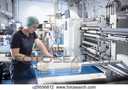 Stock Image - Worker writing notes on newly printed food packaging in print factory. Fotosearch
