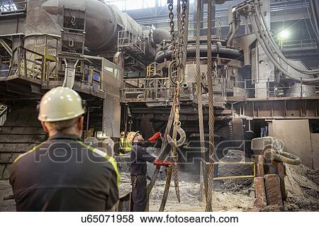 Stock Photo - Workers arranging crane lines in steelworks. Fotosearch