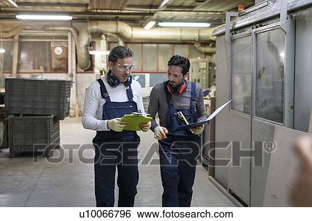 Stock Photograph - Workers discussing work in factory. Fotosearch