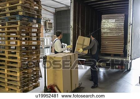 Stock Image - Workers loading boxes into truck in factory. Fotosearch