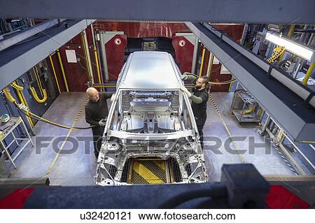 Stock Image - Workers polishing car bodies on production line in car factory. Fotosearch