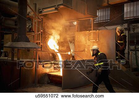 Stock Image - Workers pouring liquid titanium alloy from furnace in titanium recycling plant. Fotosearch