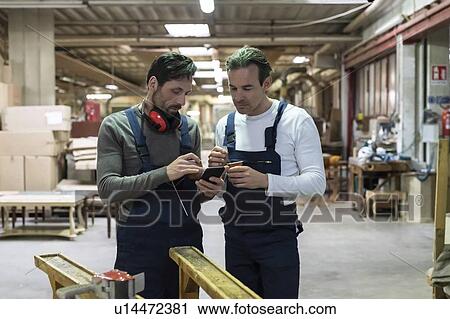 Stock Image - Workers using smartphone during coffee break in factory. Fotosearch