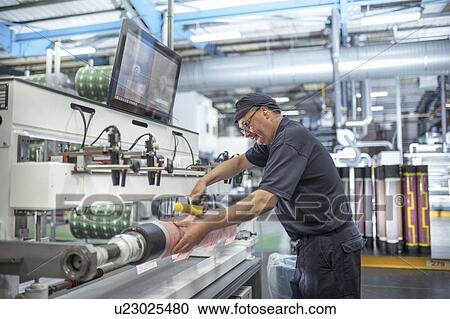 Stock Image - Working rolling on print surface in print factory. Fotosearch