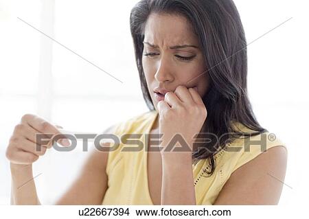 Picture - Worried woman looking at pregnancy test. Fotosearch