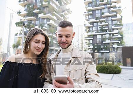 Stock Image - Young couple using smartphone in city, Milano, Lombardia, Italy. Fotosearch