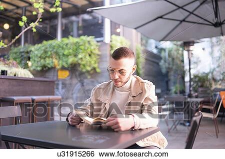 Stock Photograph - Young man reading book at cafe, Milano, Lombardia, Italy. Fotosearch