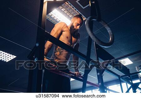 Picture - Young man training in gym, doing push ups on exercise bar. Fotosearch