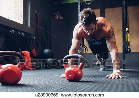 Stock Photo - Young man training in gym, doing push ups on floor. Fotosearch