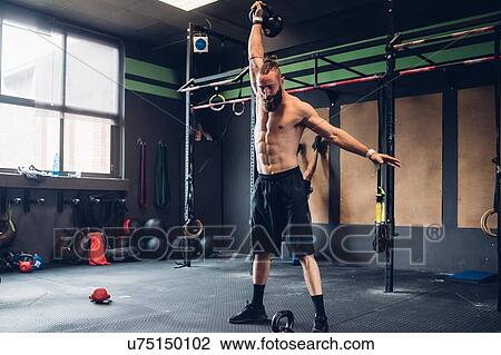 Young man training in gym, lifting kettle bell View Large Photo Image Stock Image - Young man training in gym, lifting kettle bell. Fotosearch