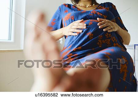 Stock Image - Young pregnant woman sitting on chair with feet up, cropped. Fotosearch