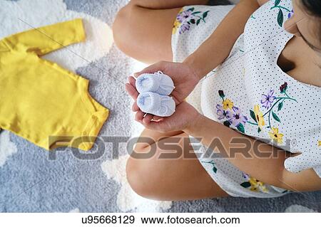Young pregnant woman sitting on floor holding baby booties, overhead view View Large Photo Image Stock Photo - Young pregnant woman sitting on floor holding baby booties, overhead view. Fotosearch