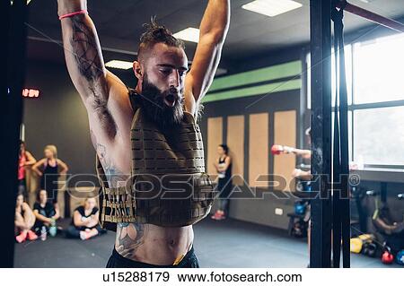 Young tattooed man training in gym, hanging from exercise bar View Large Photo Image Stock Photo - Young tattooed man training in gym, hanging from exercise bar. Fotosearch