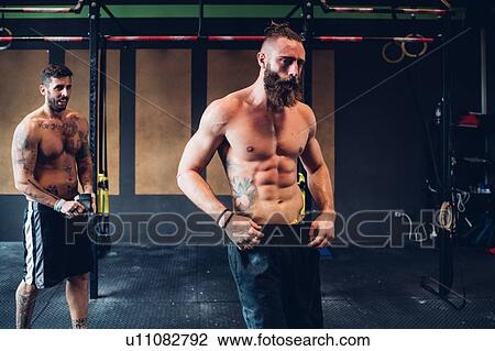 Stock Image - Young tattooed men training in gym, taking a break. Fotosearch
