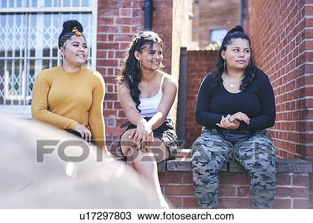 Young woman and her teenage sisters sitting on wall looking away View Large Photo Image Stock Image - Young woman and her teenage sisters sitting on wall looking away. Fotosearch
