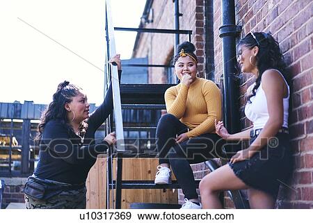 Young woman and her teenage sisters chatting on fire escape View Large Photo Image Stock Photo - Young woman and her teenage sisters chatting on fire escape. Fotosearch