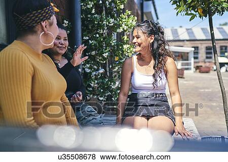 Young woman and her teenage sisters sitting on outdoor table chatting View Large Photo Image Stock Photo - Young woman and her teenage sisters sitting on outdoor table chatting. Fotosearch