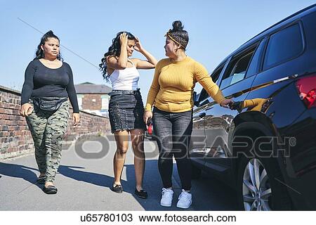 Stock Image - Young woman and two teenage sisters opening car door, UK. Fotosearch