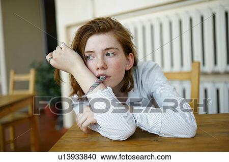Young woman biting her bracelet at table View Large Photo Image Stock Image - Young woman biting her bracelet at table. Fotosearch