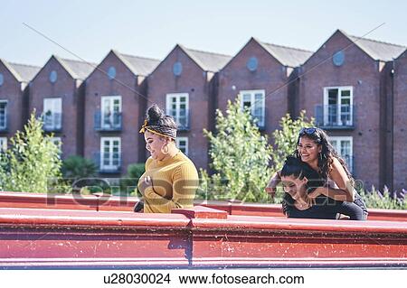 Picture - Young woman getting piggy back from teenage sister crossing footbridge. Fotosearch