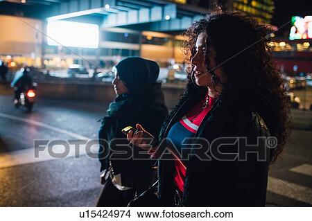 Young woman in hijab and friend on pedestrian crossing in city at night View Large Photo Image Picture - Young woman in hijab and friend on pedestrian crossing in city at night. Fotosearch