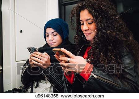 Young woman in hijab and friend sitting on subway train looking at smartphones View Large Photo Image Stock Photo - Young woman in hijab and friend sitting on subway train looking at smartphones. Fotosearch