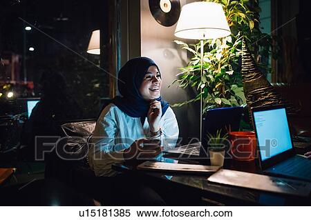 Stock Photography - Young woman in hijab at a cafe table laughing. Fotosearch