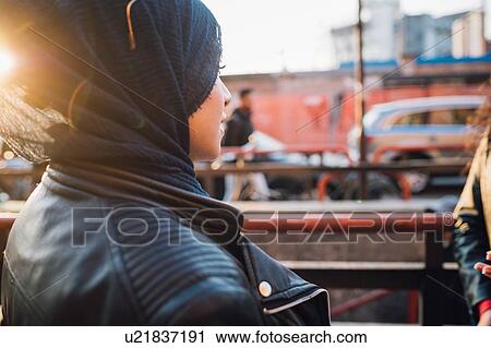 Stock Image - Young woman in hijab on city sidewalk, over shoulder view. Fotosearch