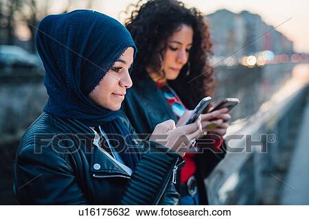 Young woman in hijab with best friend looking at smartphones by city canal View Large Photo Image Stock Image - Young woman in hijab with best friend looking at smartphones by city canal. Fotosearch