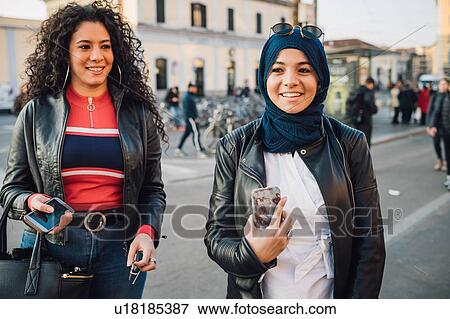 Stock Photo - Young woman in hijab with best friend on city street. Fotosearch
