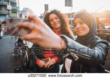 Young woman in hijab with friend taking smartphone selfie in city View Large Photo Image Stock Image - Young woman in hijab with friend taking smartphone selfie in city. Fotosearch