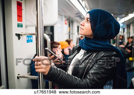 Young woman in hijab with smartphone on subway train View Large Photo Image Stock Photo - Young woman in hijab with smartphone on subway train. Fotosearch