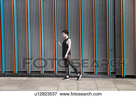 Stock Photo - Young woman in sports clothing looking at smartphone on city sidewalk. Fotosearch