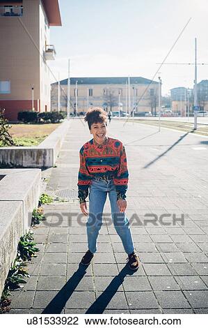 Stock Image - Young woman laughing on urban sidewalk, full length portrait. Fotosearch