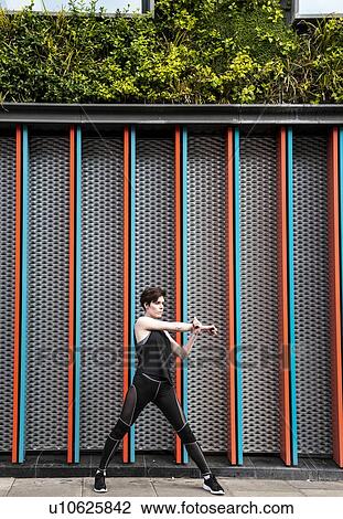 Stock Image - Young woman practicing yoga on city sidewalk, full length. Fotosearch