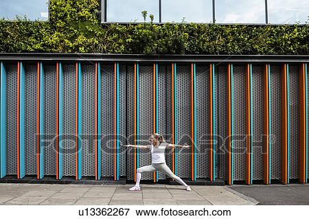 Stock Photo - Young woman practicing yoga pose on city sidewalk, arms and legs outstretched. Fotosearch