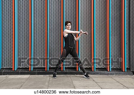 Stock Photograph - Young woman practicing yoga pose on city sidewalk, full length portrait. Fotosearch