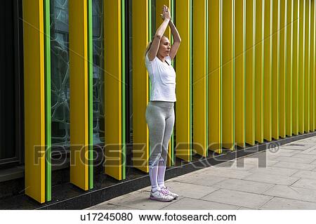 Stock Image - Young woman practicing yoga pose with hands together on city sidewalk, full length. Fotosearch