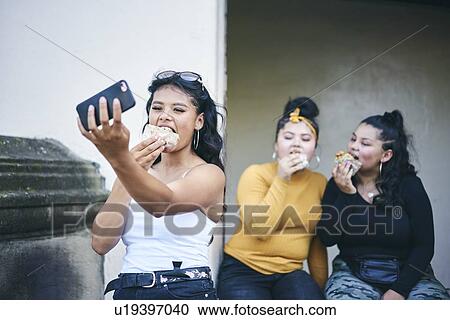 Young woman taking selfie with teenage sisters while eating cakes in doorway View Large Photo Image Stock Image - Young woman taking selfie with teenage sisters while eating cakes in doorway. Fotosearch