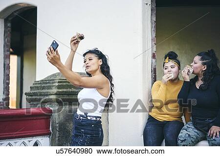Young woman taking selfie with teenage sisters while eating cakes in doorway View Large Photo Image Stock Image - Young woman taking selfie with teenage sisters while eating cakes in doorway. Fotosearch