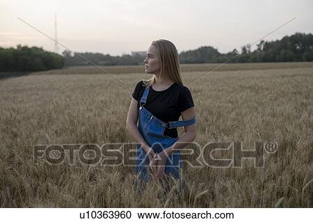Stock Image - Young woman wearing overalls in wheat field. Fotosearch