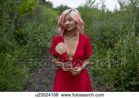 Stock Photo - Young woman wearing red dress holding seed head. Fotosearch