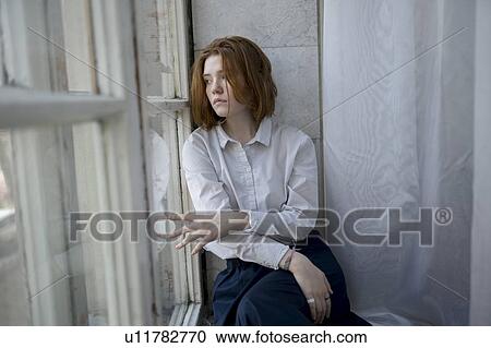 Stock Image - Young woman wearing white shirt on window sill. Fotosearch