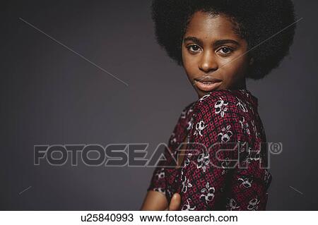 Stock Image - Young woman with afro hair against grey background. Fotosearch
